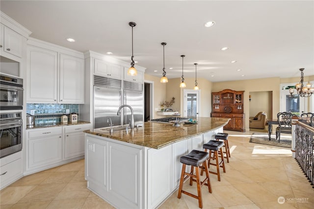 kitchen featuring appliances with stainless steel finishes, white cabinetry, sink, dark stone counters, and a center island with sink