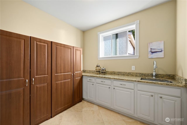 kitchen featuring light stone countertops, sink, light tile patterned floors, and white cabinets