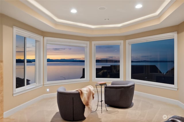 living area with a raised ceiling, a water view, and light carpet