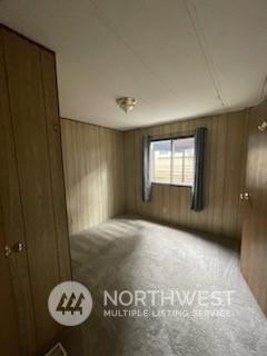 carpeted spare room with wooden walls