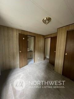 unfurnished bedroom with carpet and wood walls