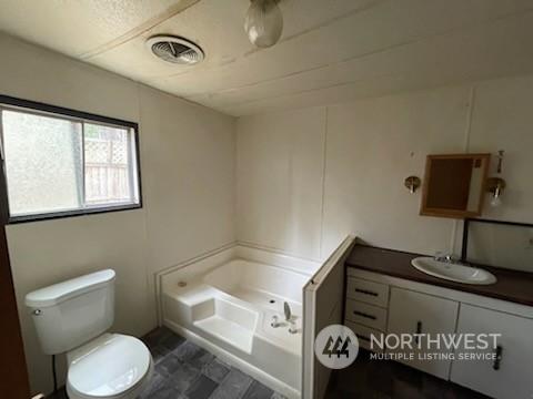 bathroom featuring a tub to relax in, toilet, and vanity