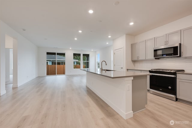 29209 217th Pl SE Unit 30, Black Diamond, WA 98010 - kitchen with appliances with stainless steel finishes, light wood-style flooring, a center island with sink, decorative backsplash, and a sink