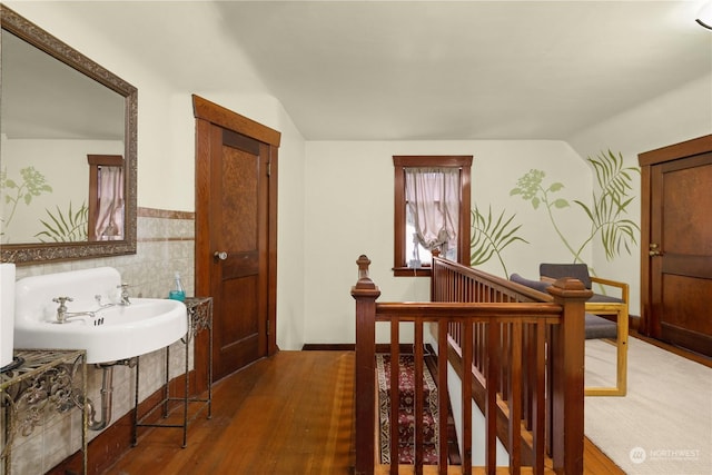 hallway featuring lofted ceiling, sink, hardwood / wood-style floors, and tile walls