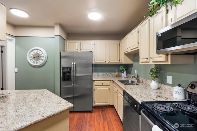 kitchen with appliances with stainless steel finishes, sink, light stone countertops, dark wood-type flooring, and cream cabinetry