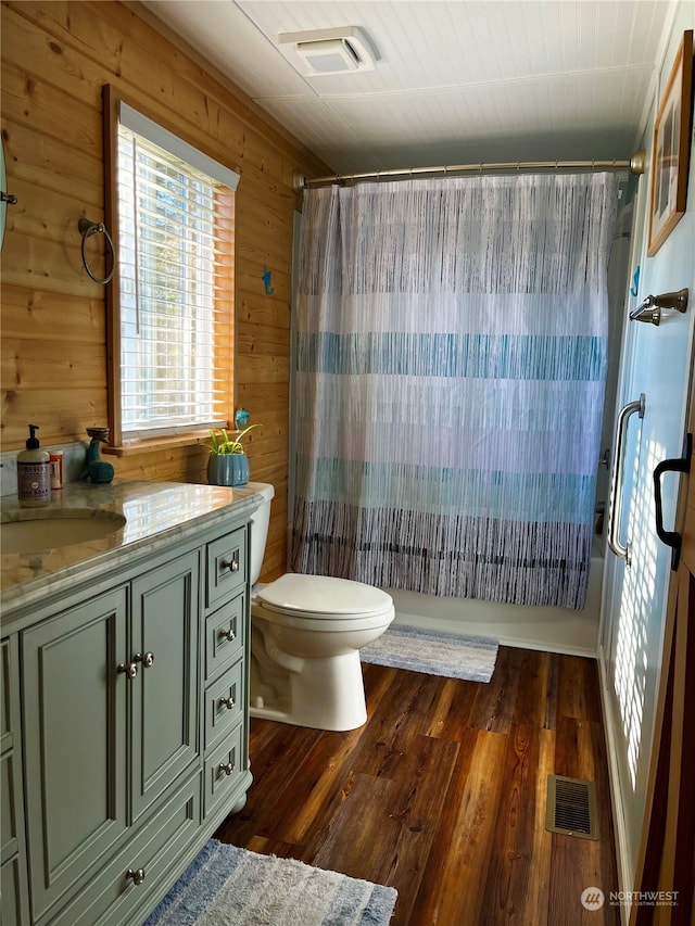 bathroom with a shower with shower curtain, hardwood / wood-style floors, vanity, wooden walls, and toilet