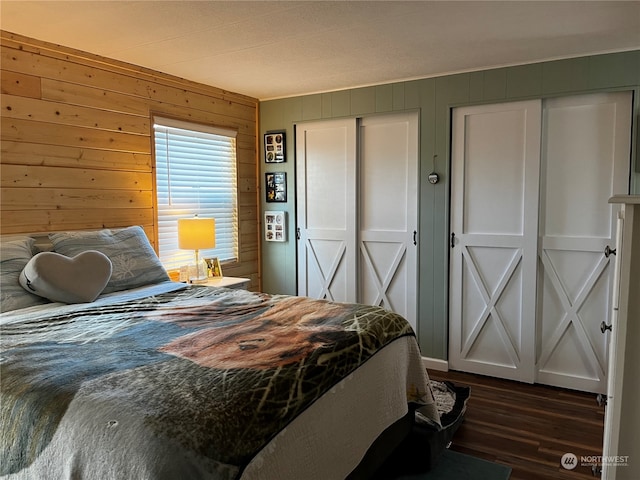 bedroom featuring multiple closets, dark hardwood / wood-style flooring, and wooden walls