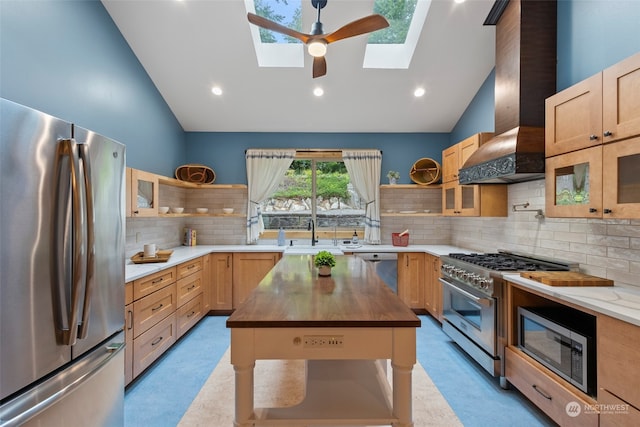 kitchen featuring stainless steel appliances, tasteful backsplash, wall chimney range hood, and a skylight