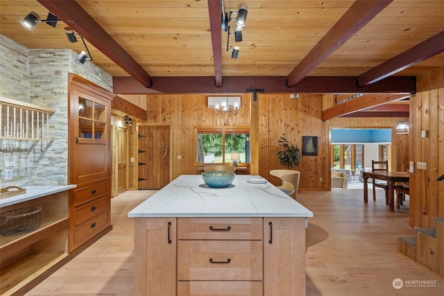 kitchen featuring rail lighting, light stone counters, a center island, wooden walls, and beamed ceiling