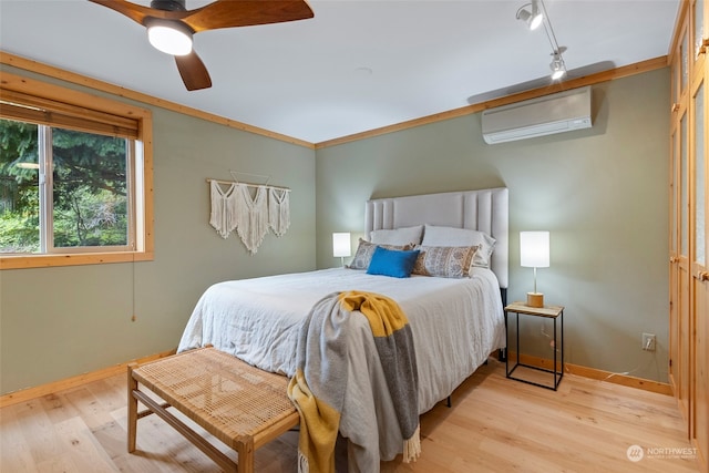 bedroom with a wall mounted air conditioner, rail lighting, ornamental molding, ceiling fan, and light hardwood / wood-style floors