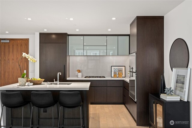 kitchen featuring light hardwood / wood-style flooring, sink, gas stovetop, stainless steel oven, and a kitchen breakfast bar