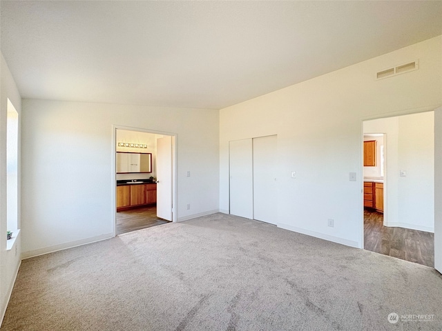 unfurnished bedroom featuring a closet, ensuite bath, and carpet floors