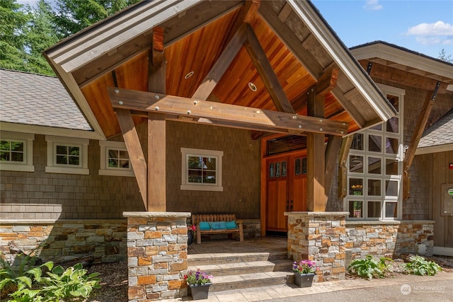 doorway to property with stone siding, covered porch, and a shingled roof