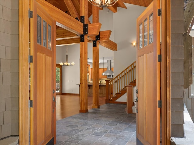 foyer featuring high vaulted ceiling, stone finish floor, a chandelier, baseboards, and stairs