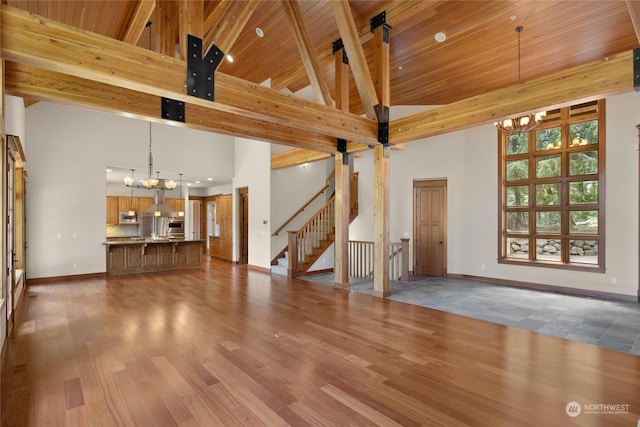 unfurnished living room featuring baseboards, wood ceiling, wood finished floors, a high ceiling, and a notable chandelier