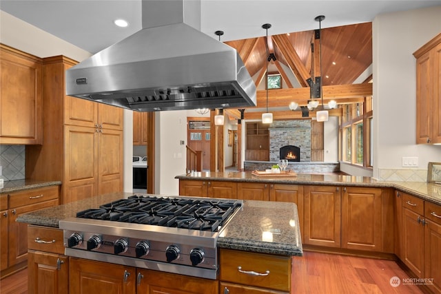 kitchen with brown cabinets, stainless steel gas cooktop, ventilation hood, and dark stone counters