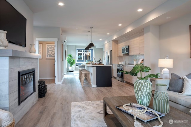 living room featuring a wall mounted air conditioner, light hardwood / wood-style flooring, and a tile fireplace