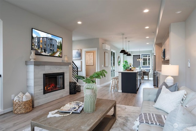 living room with a tiled fireplace, sink, light hardwood / wood-style floors, and an AC wall unit