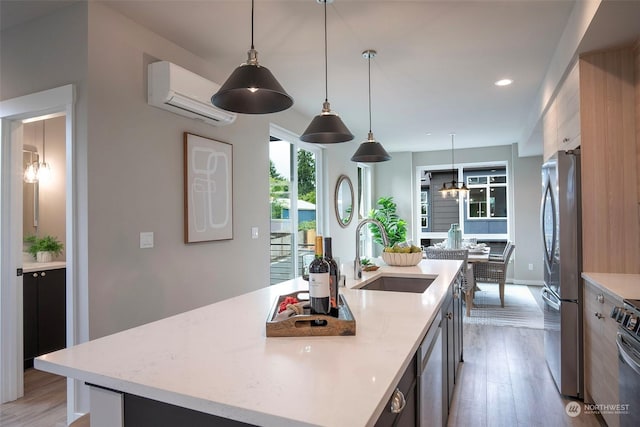 kitchen with pendant lighting, sink, appliances with stainless steel finishes, a kitchen island with sink, and a wall mounted air conditioner