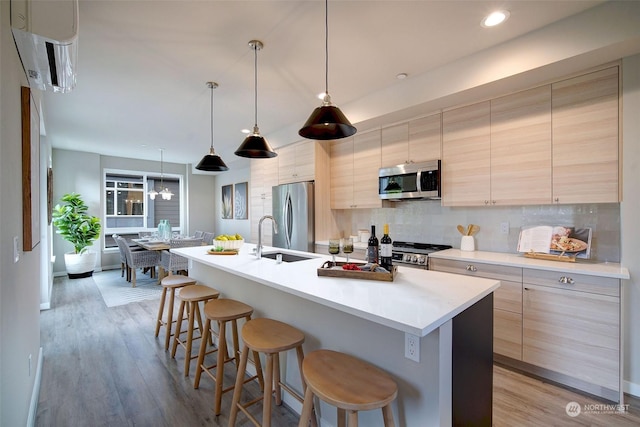 kitchen featuring pendant lighting, sink, backsplash, a kitchen island with sink, and stainless steel appliances