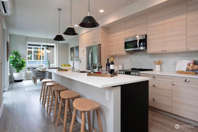 kitchen with sink, light brown cabinets, an island with sink, stainless steel appliances, and backsplash