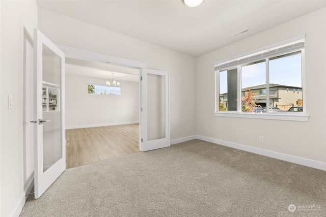 spare room with carpet floors, a notable chandelier, and french doors