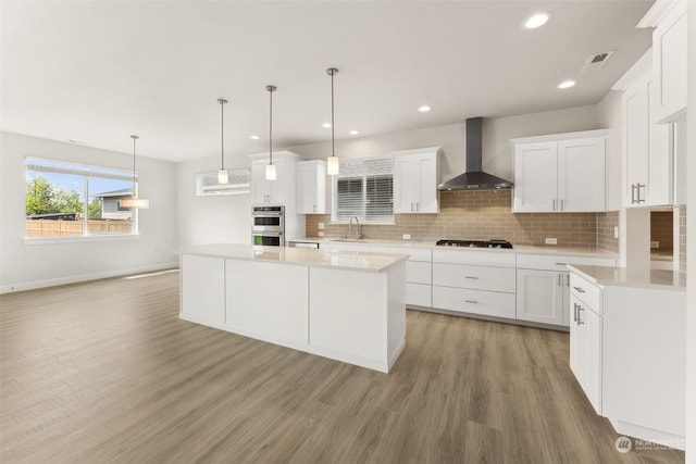 kitchen with white cabinetry, decorative light fixtures, sink, and wall chimney range hood