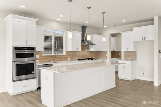 kitchen featuring wall chimney exhaust hood, sink, white cabinetry, appliances with stainless steel finishes, and a kitchen island