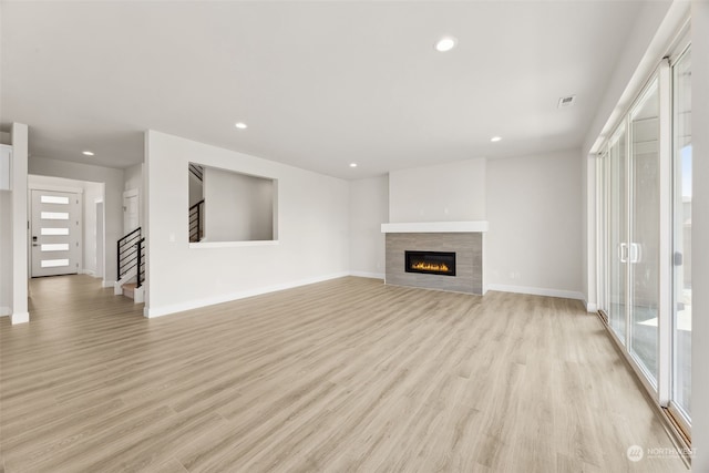 unfurnished living room with a tile fireplace, a healthy amount of sunlight, and light hardwood / wood-style flooring