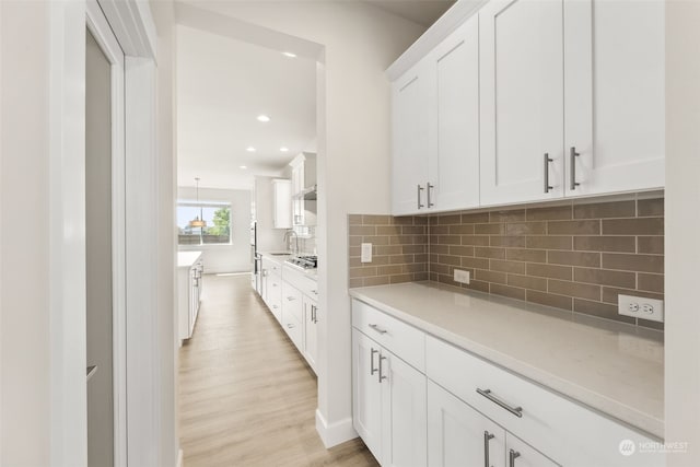 kitchen featuring sink, light hardwood / wood-style flooring, tasteful backsplash, white cabinets, and stainless steel gas stovetop