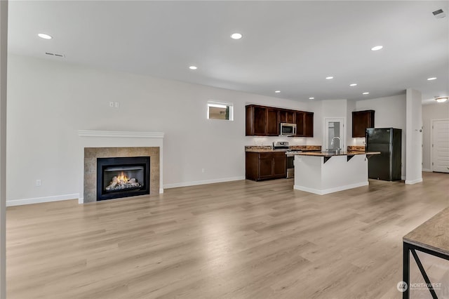 kitchen with sink, a breakfast bar, stainless steel appliances, light hardwood / wood-style floors, and a center island with sink