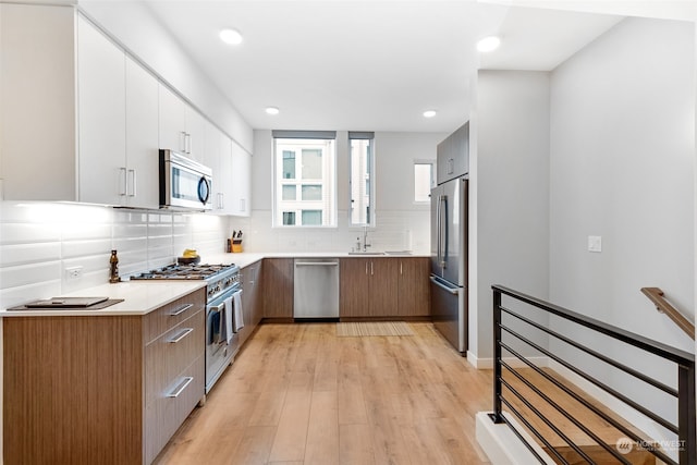 kitchen featuring stainless steel appliances, decorative backsplash, white cabinets, light wood-type flooring, and sink