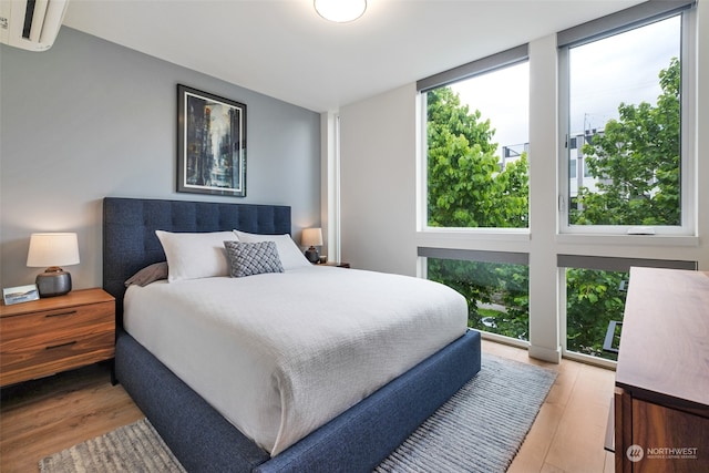 bedroom featuring an AC wall unit, multiple windows, and light hardwood / wood-style floors