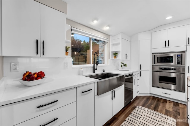 kitchen with tasteful backsplash, stainless steel appliances, white cabinetry, sink, and dark wood-type flooring