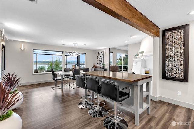 kitchen with dark wood-type flooring, hanging light fixtures, a kitchen bar, beam ceiling, and a chandelier