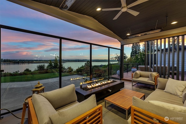 patio terrace at dusk featuring an outdoor living space with a fire pit, a water view, and ceiling fan