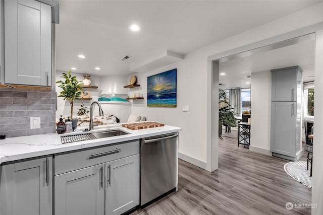 kitchen with gray cabinets, stainless steel dishwasher, light hardwood / wood-style floors, backsplash, and sink