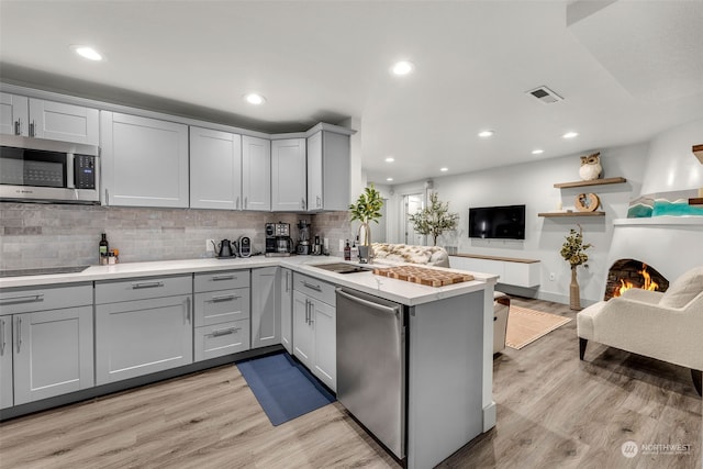 kitchen featuring gray cabinetry, light wood-type flooring, appliances with stainless steel finishes, and kitchen peninsula