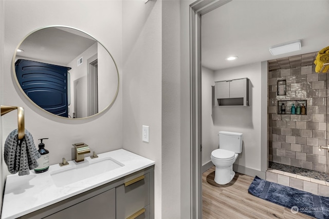 bathroom with toilet, a tile shower, vanity, and hardwood / wood-style flooring