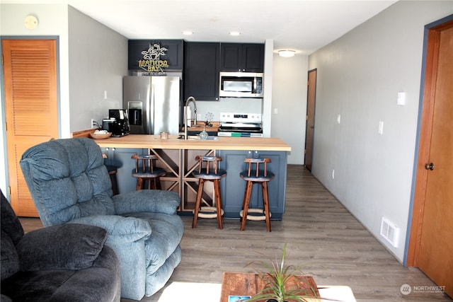 kitchen featuring a breakfast bar, butcher block counters, kitchen peninsula, stainless steel appliances, and light hardwood / wood-style floors