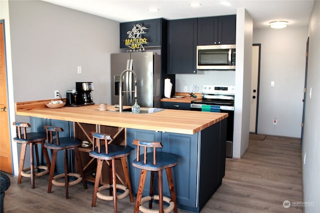 kitchen with a kitchen bar, appliances with stainless steel finishes, hardwood / wood-style floors, and butcher block counters