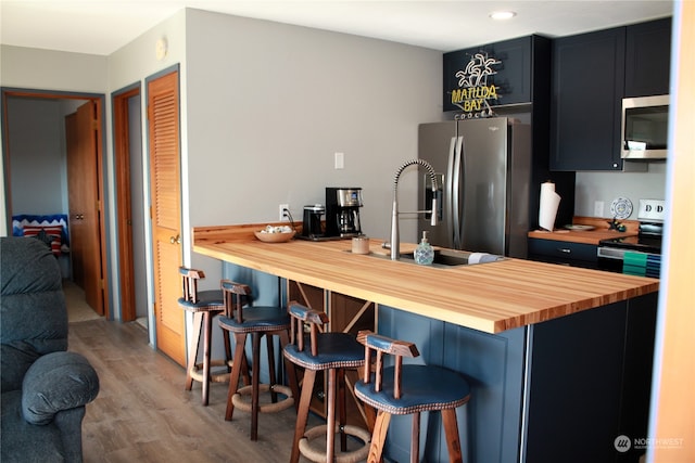 kitchen with stove, wood counters, a breakfast bar, fridge, and hardwood / wood-style flooring