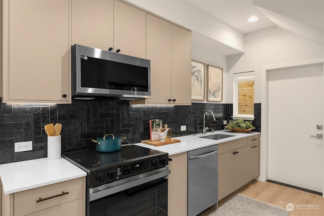 kitchen featuring appliances with stainless steel finishes, decorative backsplash, sink, light wood-type flooring, and cream cabinetry