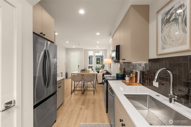 kitchen with appliances with stainless steel finishes, sink, backsplash, light wood-type flooring, and cream cabinetry