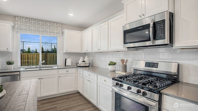 kitchen featuring sink, appliances with stainless steel finishes, decorative backsplash, white cabinets, and light wood-type flooring