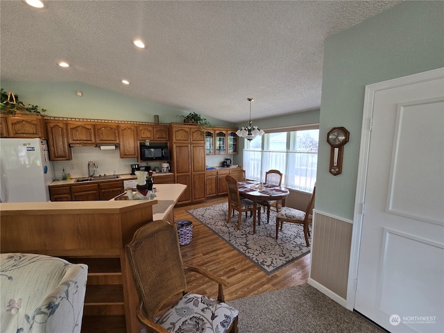 kitchen with lofted ceiling, hanging light fixtures, sink, white fridge, and hardwood / wood-style floors