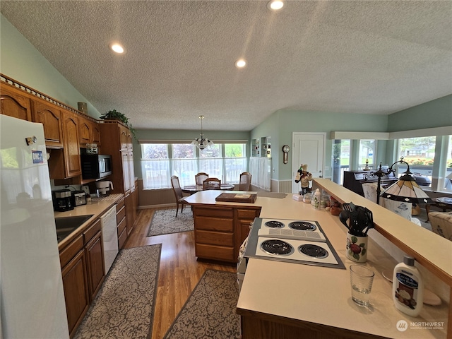 kitchen featuring lofted ceiling, white appliances, a textured ceiling, decorative light fixtures, and hardwood / wood-style flooring