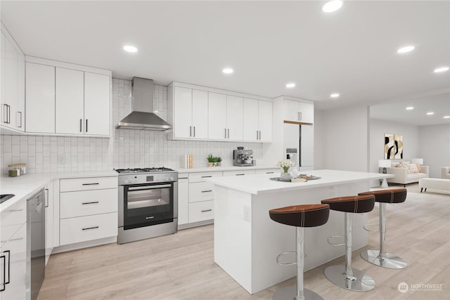 kitchen featuring a kitchen island, appliances with stainless steel finishes, white cabinets, wall chimney range hood, and light hardwood / wood-style flooring