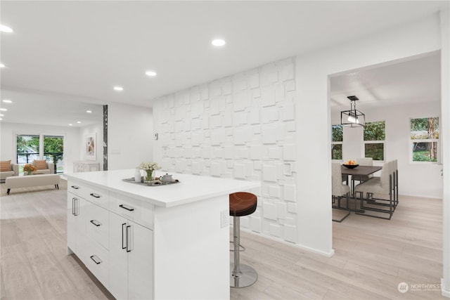 kitchen featuring white cabinetry, a kitchen bar, hanging light fixtures, a center island, and light hardwood / wood-style flooring