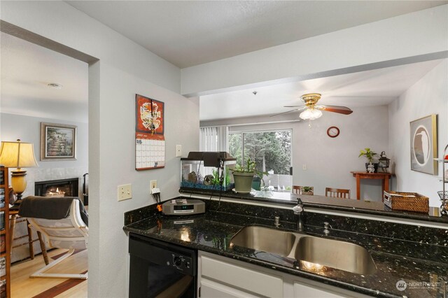 kitchen with ceiling fan, sink, dark stone countertops, dishwasher, and light hardwood / wood-style flooring